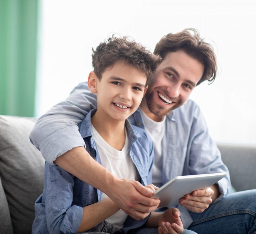 family-time-happy-dad-and-son-using-digital-tablet-browsing-internet-online-at-home-sitting-e1632233068896 (1)